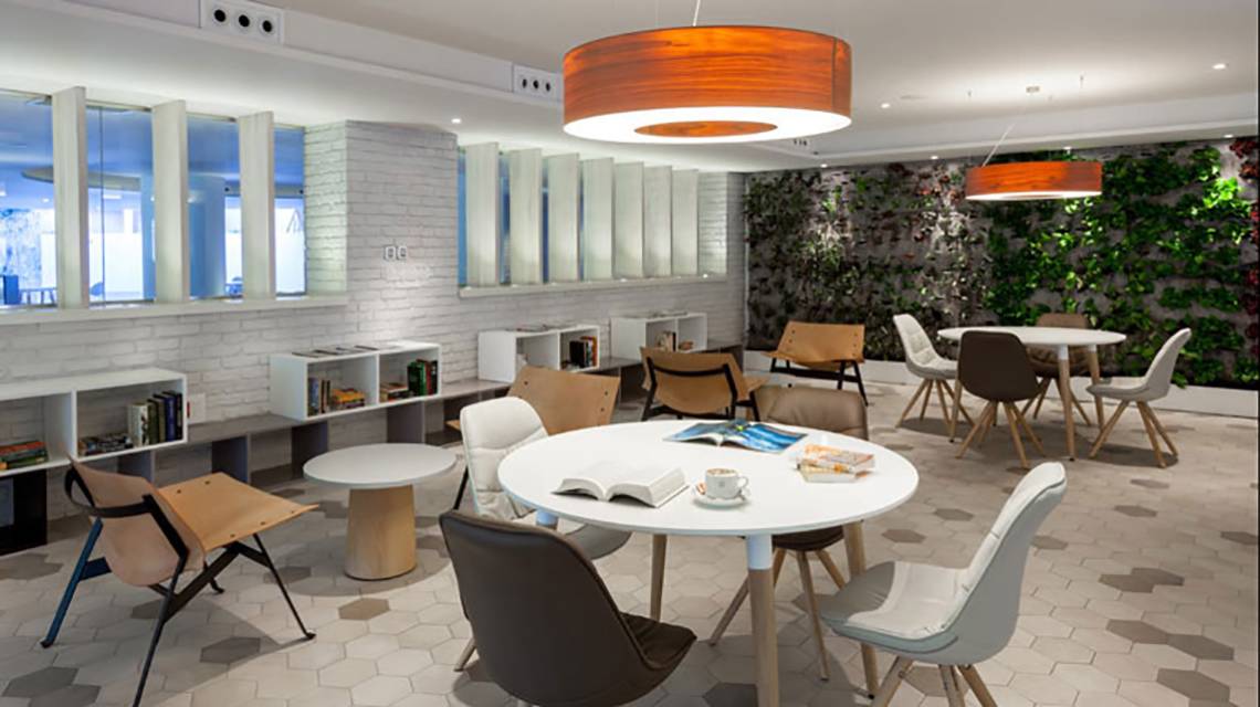 Loungebereich im Hotel Tigotan Lovers & Friends mit weißen Möbeln, grüner Wand und mehreren Tischen.