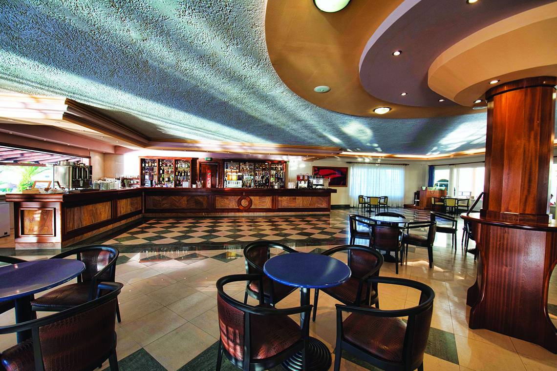 Innenbereich der Rezeption des Eurovillage Achilleas Hotels mit gemustertem Boden und runden Tischen.