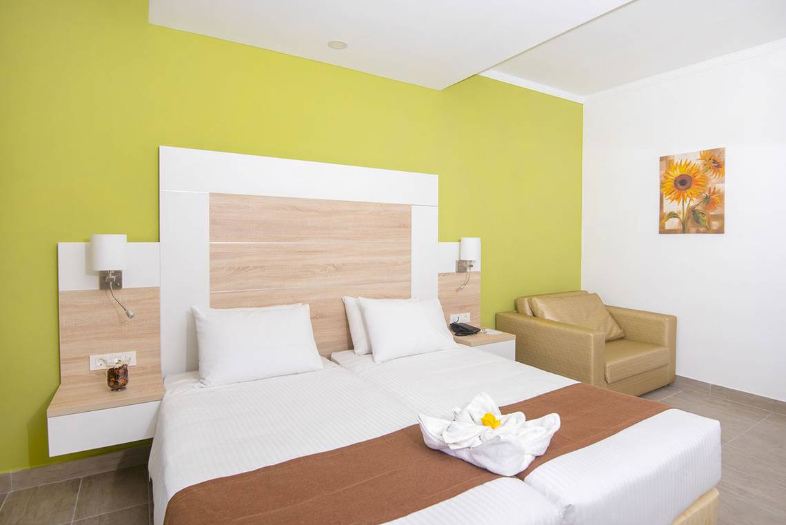 Doppelbett-Zimmer im Eurovillage Achilleas Hotel mit grüner Wand und beigem Stuhl.