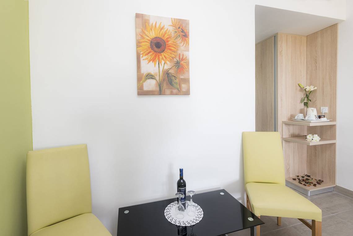 Innenansicht des Eurovillage Achilleas Hotels mit gelben Stühlen, schwarzem Tisch und Sonnenblumen-Kunstwerk an der Wand.