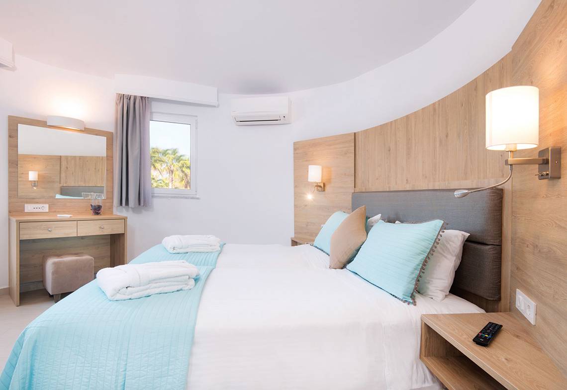 Schlafzimmer im Eurovillage Achilleas Hotel mit zwei Betten, Holzwand, Klimaanlage und Bettwäsche.