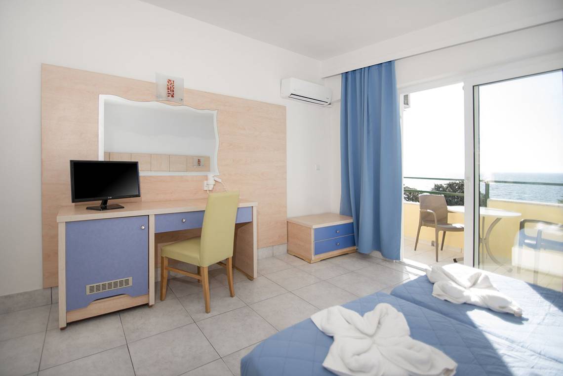 Zimmer im Eurovillage Achilleas mit Schreibtisch, Stühlen und Blick auf den Balkon.