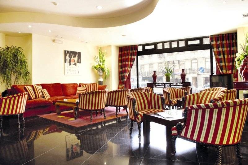 Empfangsbereich des Mundial Hotels mit roten und gelben Stühlen, einem roten Sofa und einem großen Fenster.