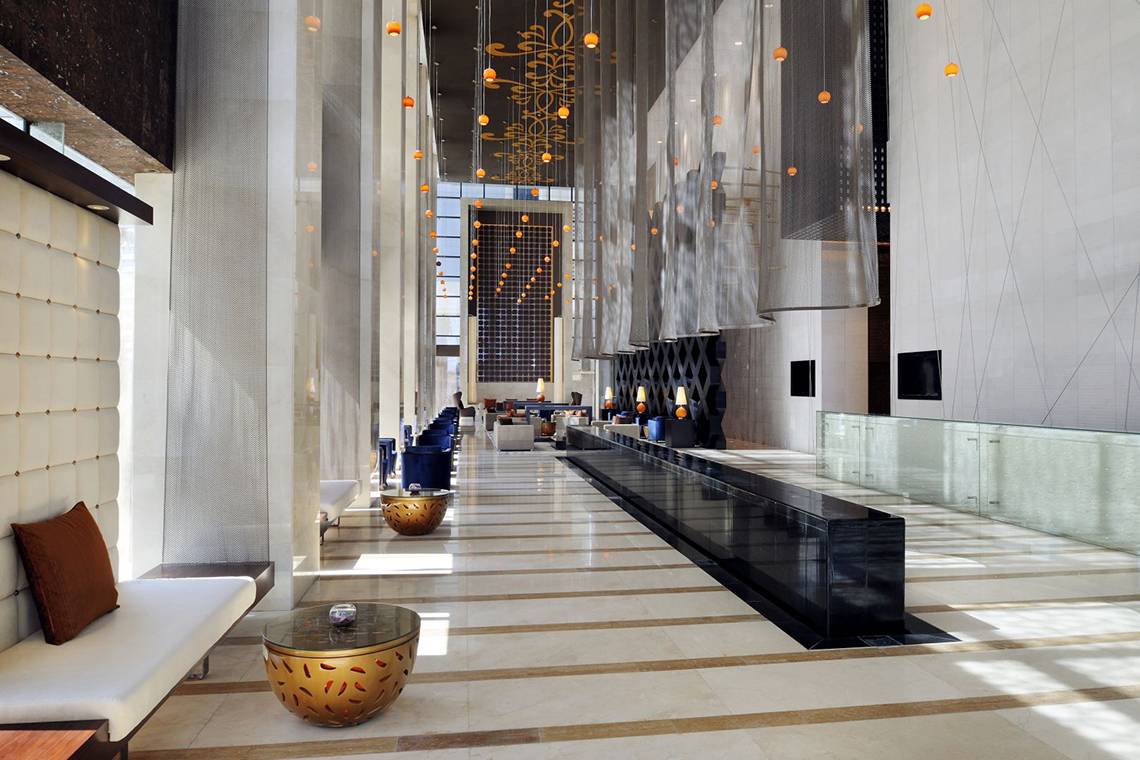 Lobby des Southern Sun Abu Dhabi Hotels mit Marmorboden, Sitzecken und orangefarbenen Pendelleuchten.