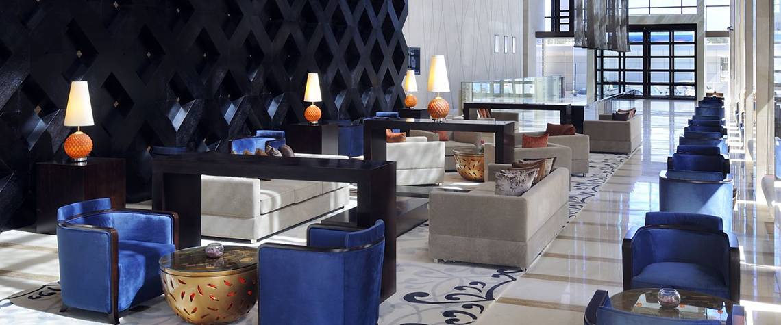 Lobby des Southern Sun Abu Dhabi Hotels mit schwarzen Wänden, weißen Sofas und blauen Sesseln.