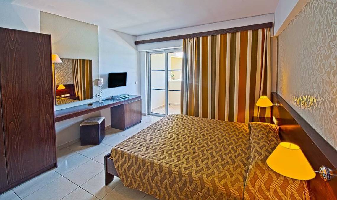 Innenansicht eines Hotelzimmers im Akti Beach Club mit Bett, Schreibtisch und Fernseher.