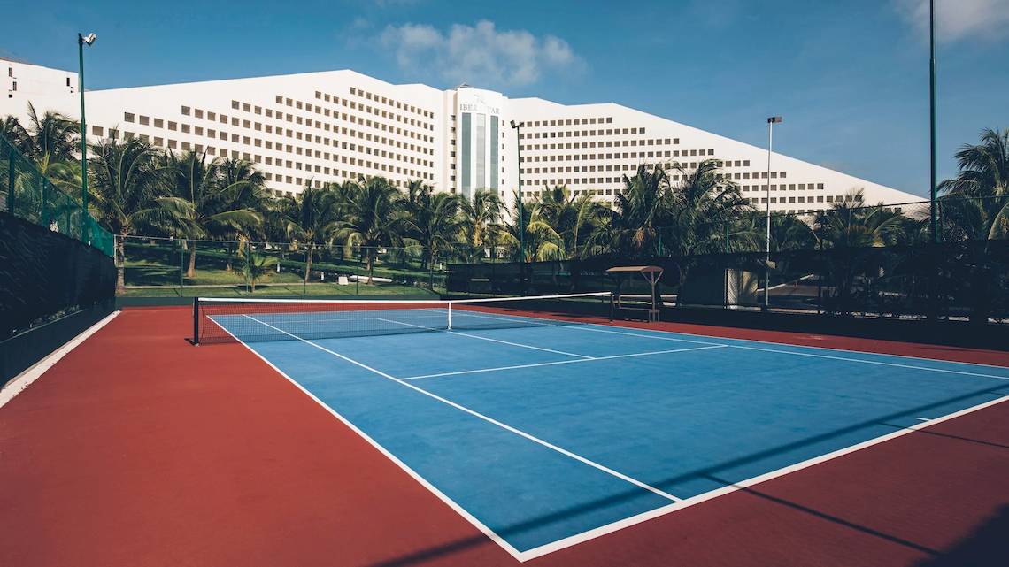 Tennisplatz vor dem Iberostar Selection Cancun Hotel mit großen Gebäuden und Palmen im Hintergrund.