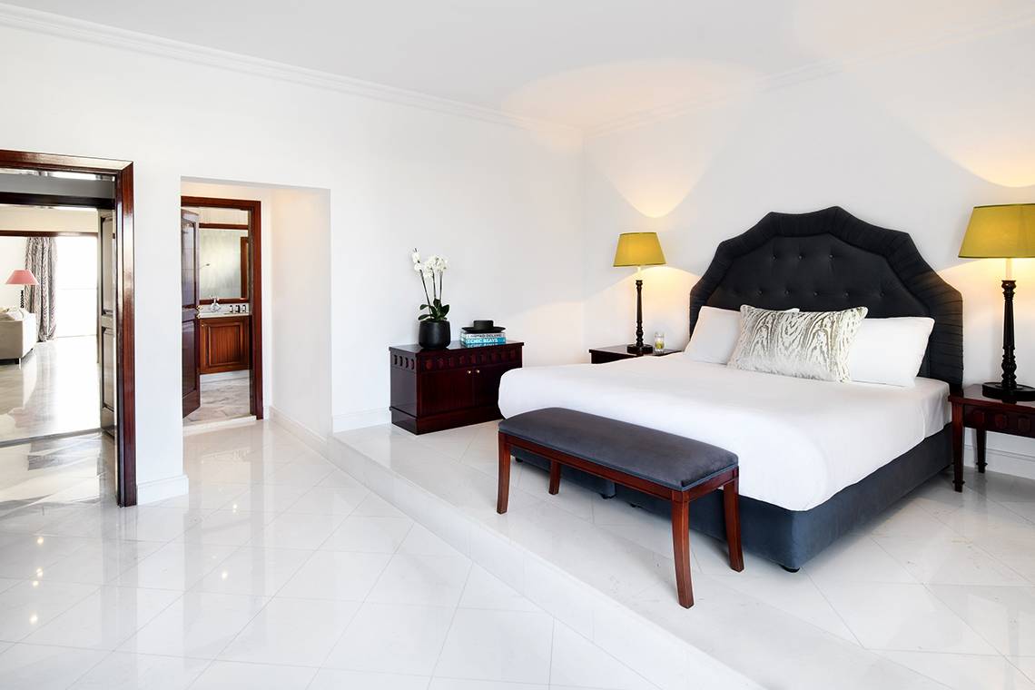 Schlafzimmer-Innenansicht des Mitsis Grand Hotel Beach mit weißem Bett, Dekor und offenen Türen.