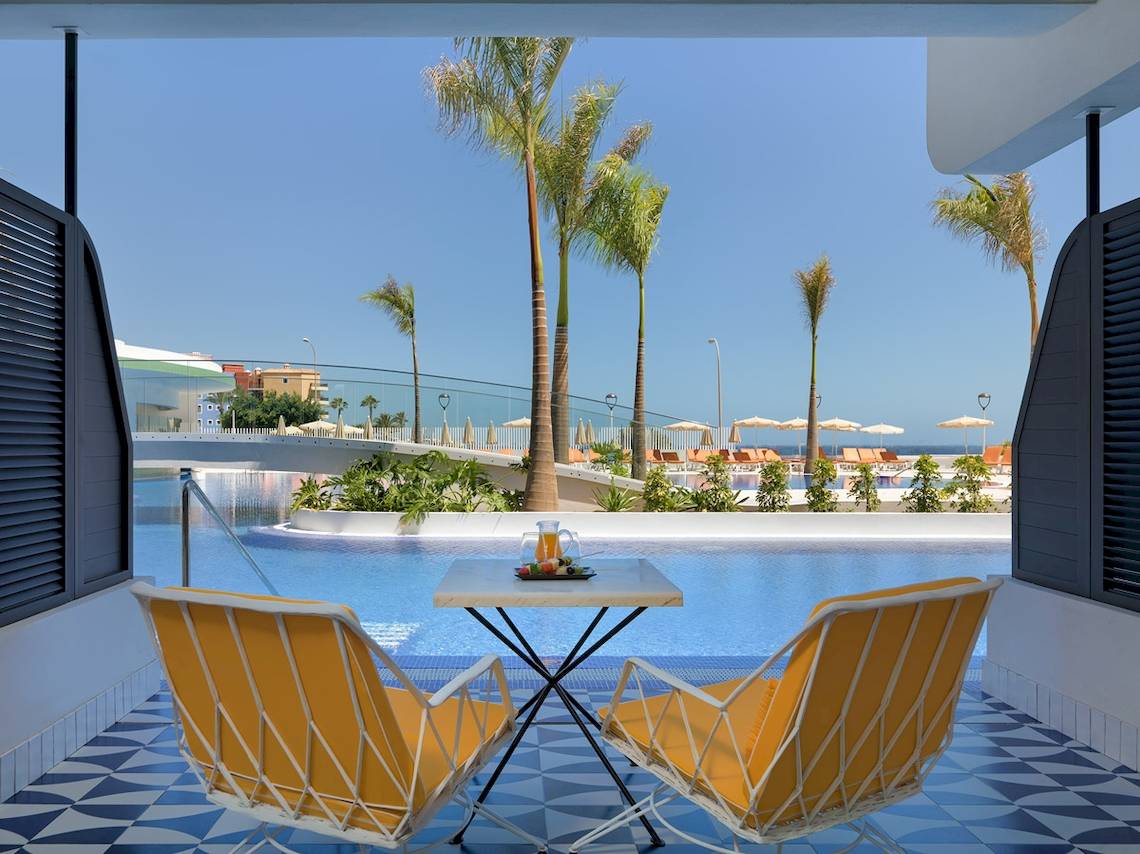 Blick auf den Poolbereich des H10 Atlantic Sunset Hotels mit zwei gelben Stühlen und einem Tisch.