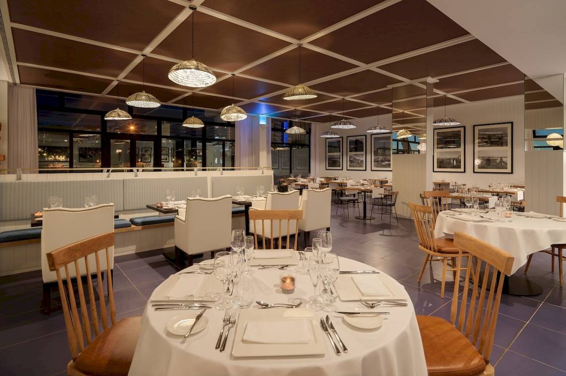 Restaurantbereich im H10 Atlantic Sunset Hotel mit weißen Tischen, Holzstühlen und Deckenlampen.