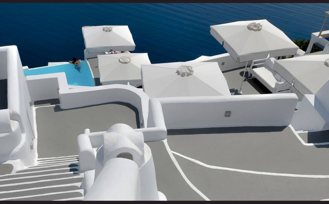 Oberirdisches Hotel mit Pool und Meerblick auf Santorini, weiß gekleidete Terrasse.