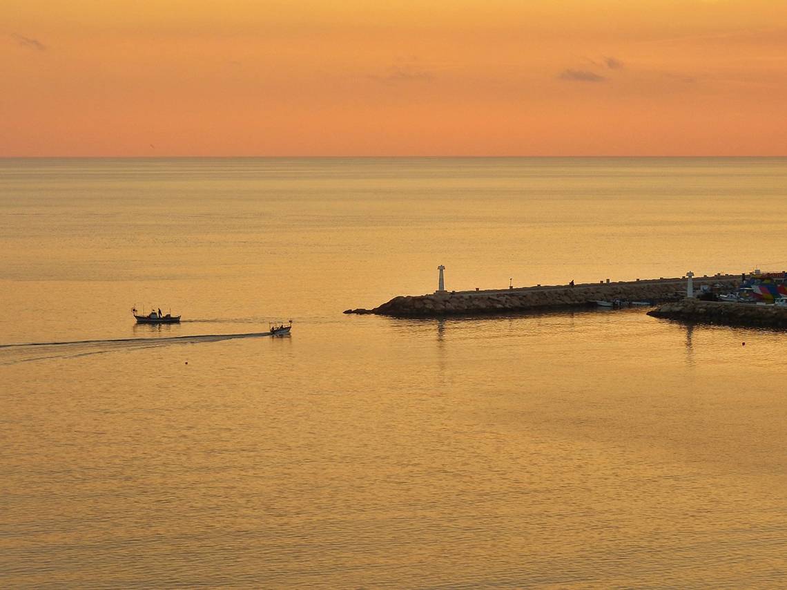 Sonnenuntergang am Wasser mit zwei Booten und einem Leuchtturm am Grecian Bay Hotel
