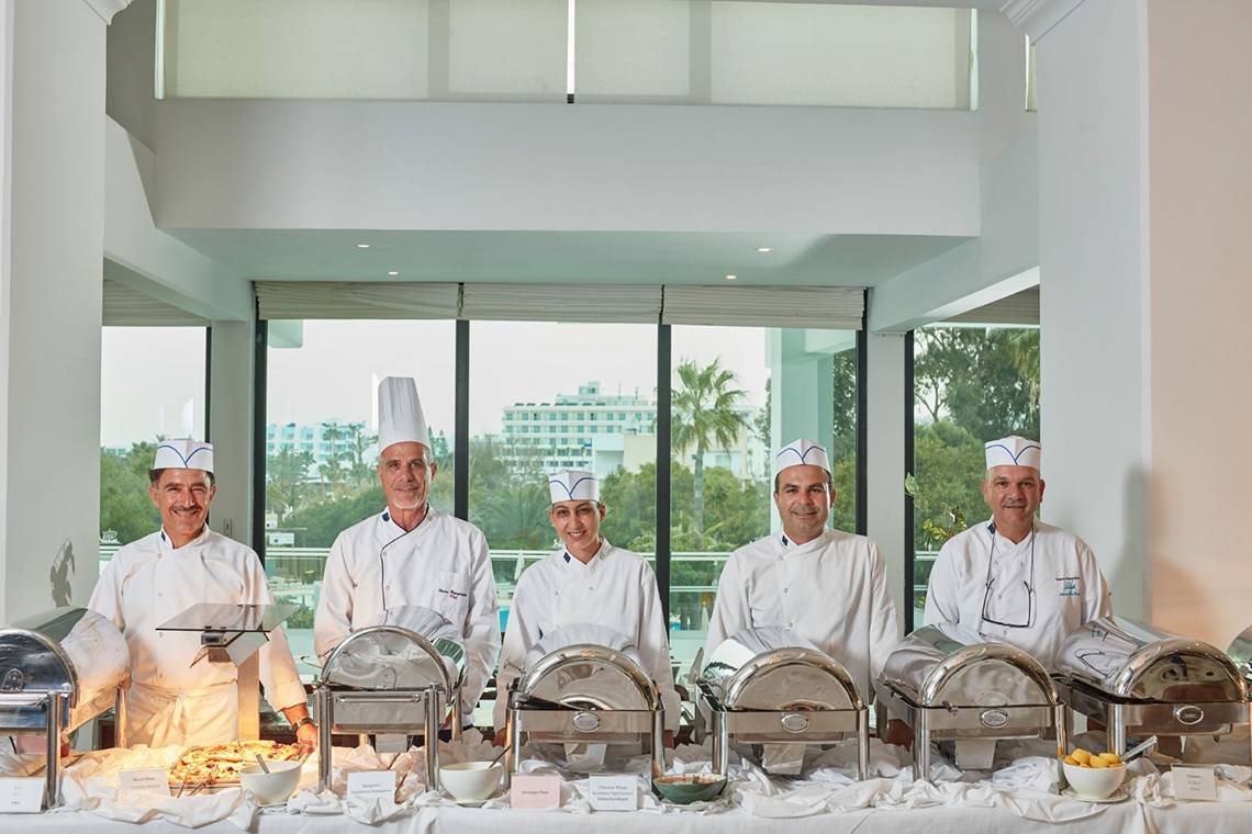 Team der Grecian Bay Hotel Küche mit Gerichten auf einem Buffet.