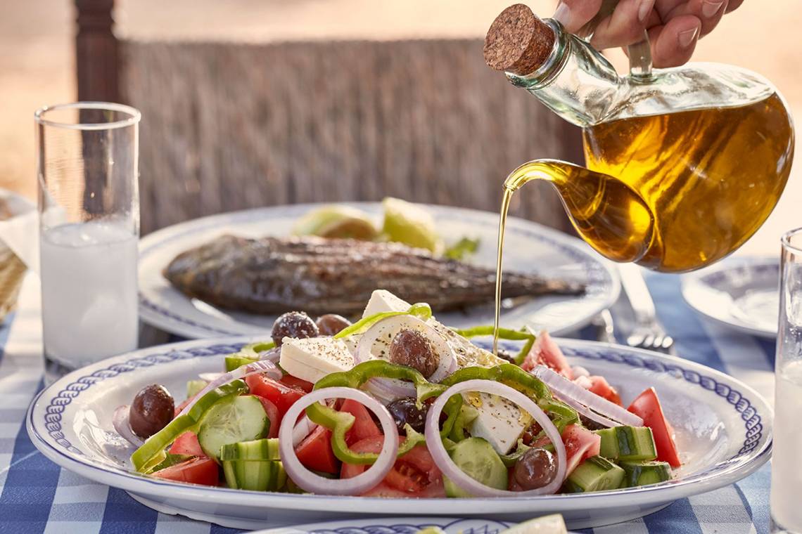 Griechisches Frühstück mit Salat und Fisch auf einem Tisch im Freien.