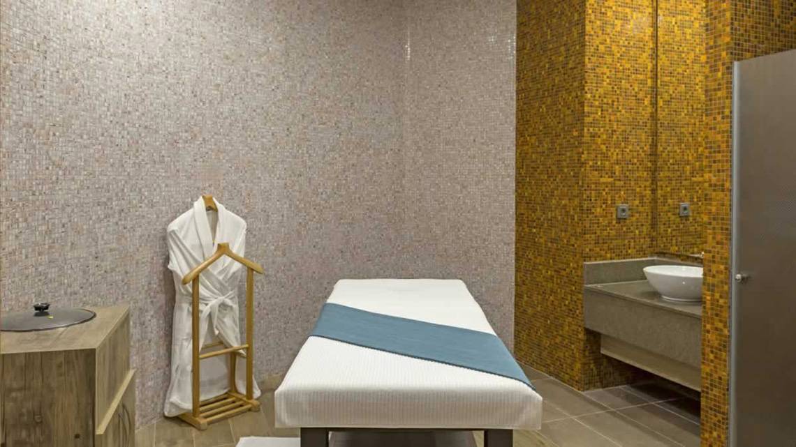Massageraum im Royal Seginus Hotel mit einem Behandlungstisch, einem Bademantel und einem Waschbecken.