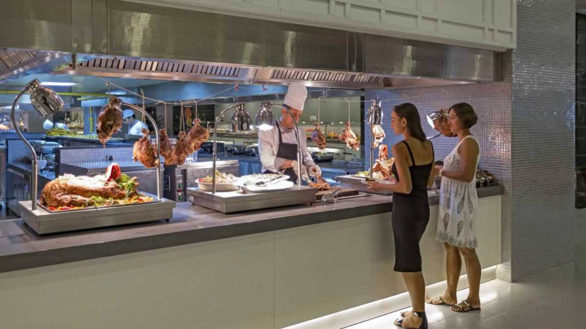 Gastronomiebereich des Royal Seginus Hotels mit einem Koch und Gästen an der Fleischtheke.