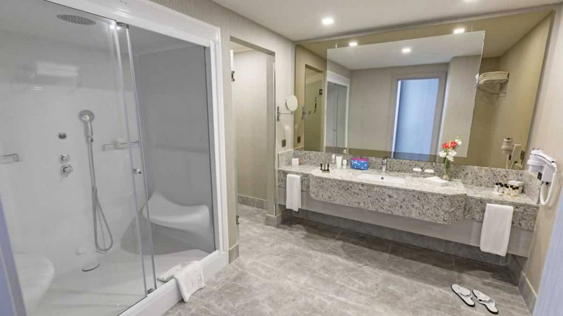 Badezimmer im Royal Seginus Hotel mit einer Dusche, Waschbecken und einem großen Spiegel.