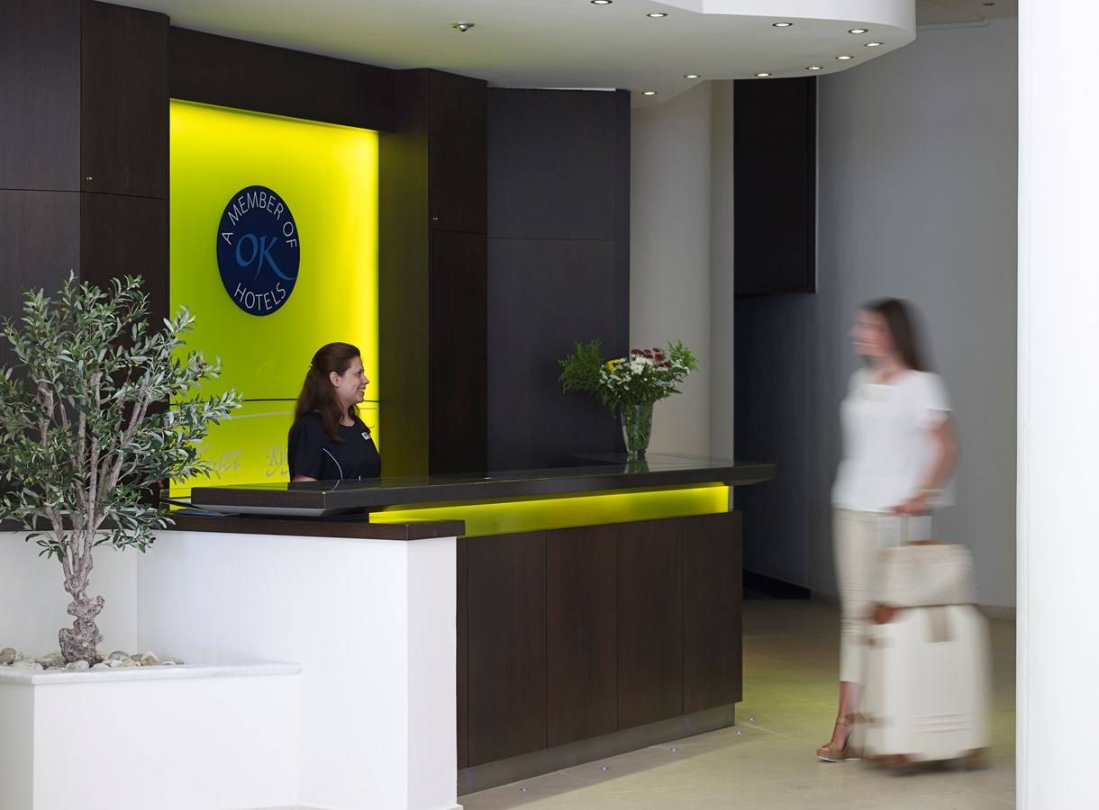 Empfang des Kriti Beach Hotels mit Rezeptionistin und Gast, die mit Gepäck unterwegs ist.