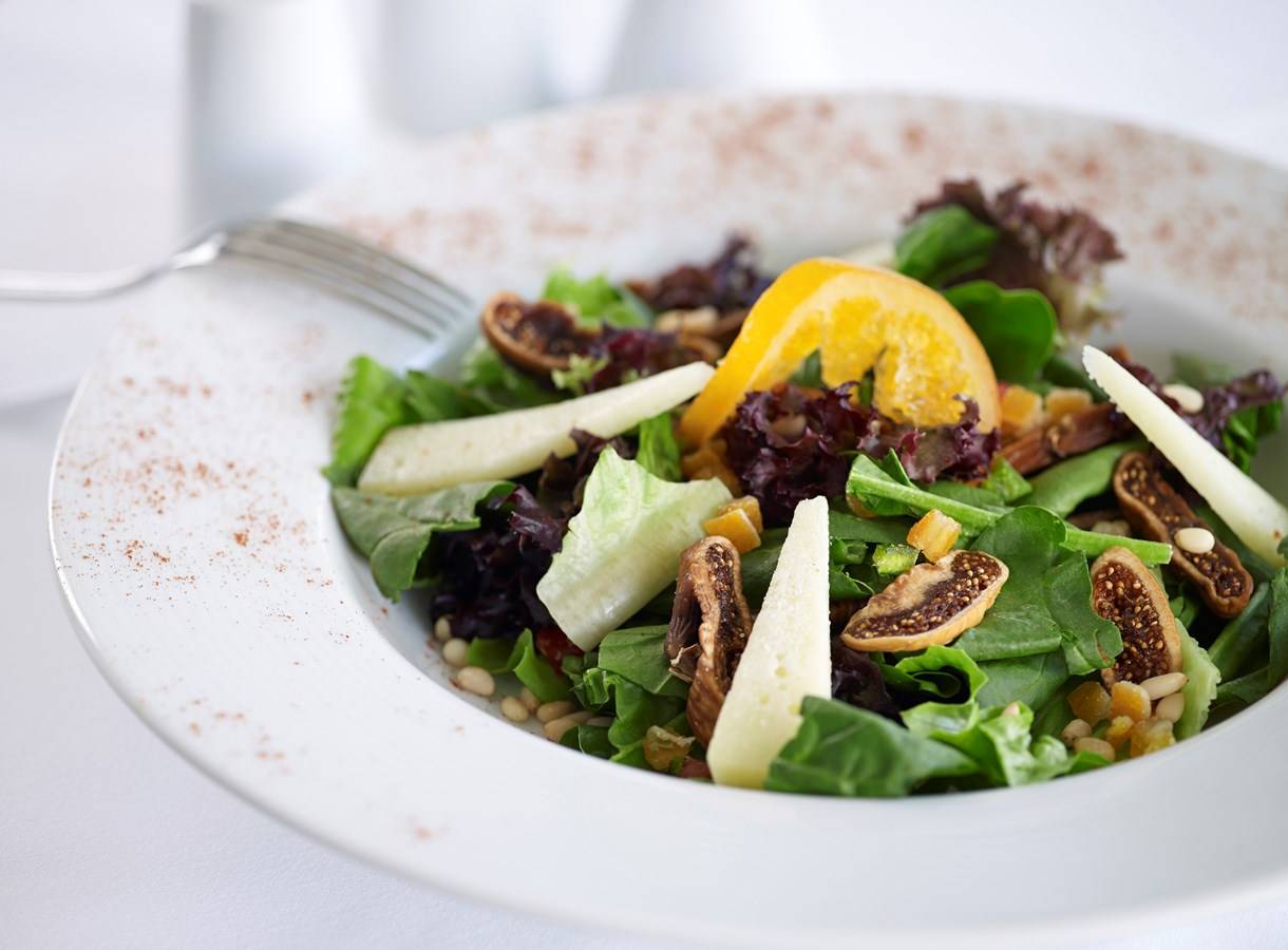 Salat in einem weißen Teller mit Obst und Nüssen.