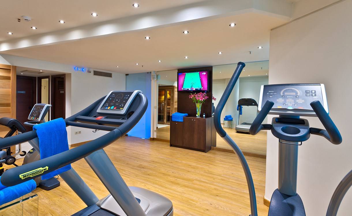 Fitnessraum im Kriti Beach Hotel mit Laufband, Fernseher und Trainingsgeräten.
