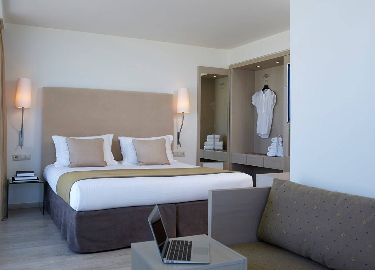 Schlafzimmer im Kriti Beach Hotel mit Doppelbett, Nachttischen und Laptop auf Beistelltisch.
