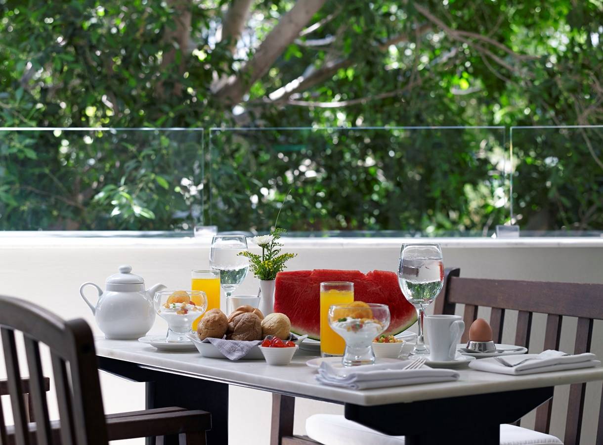 Frühstückstisch mit Obst und Getränken auf einer Terrasse mit Blick auf Bäume.