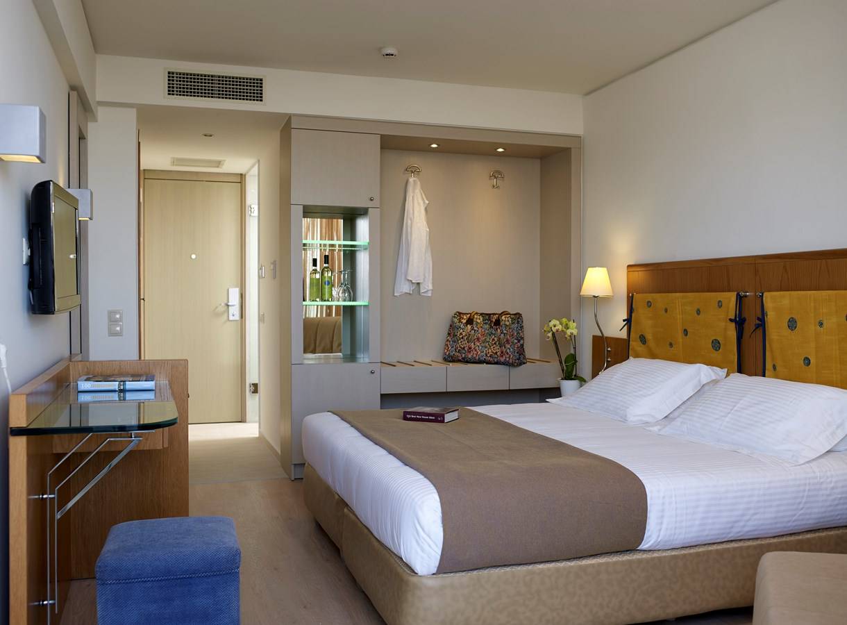 Ein elegantes Hotelzimmer im Kriti Beach Hotel mit einem großen Bett und einem Schreibtisch.