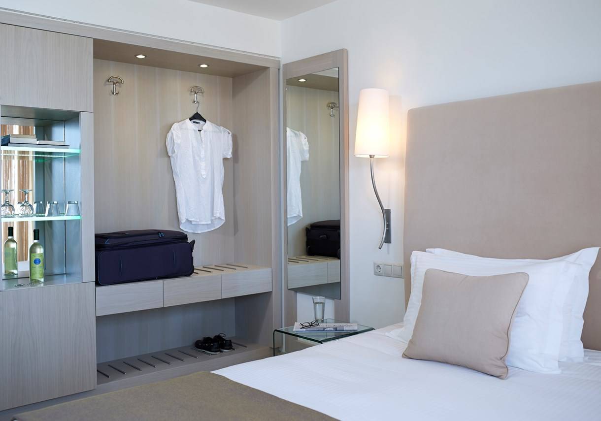 Schlafzimmer im Kriti Beach Hotel mit Bett, Kissen, Lampe und Kleiderschrank.