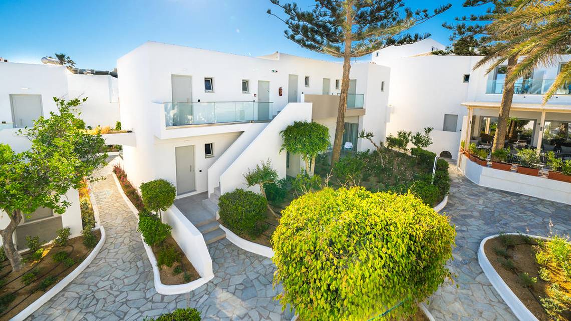 Außenansicht des Adele Beach Hotels mit weißen Gebäuden, Treppen und gepflegten Gärten.