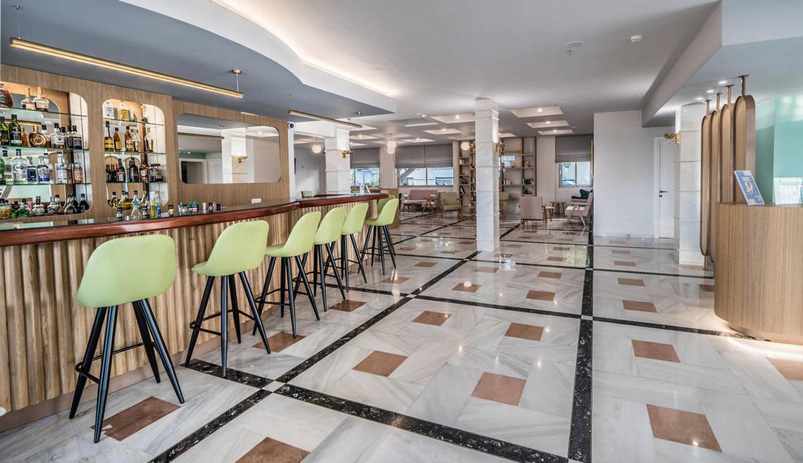 Innenansicht der Bar im Adele Beach Hotel mit grünen Stühlen und einer Theke voller Alkoholflaschen.
