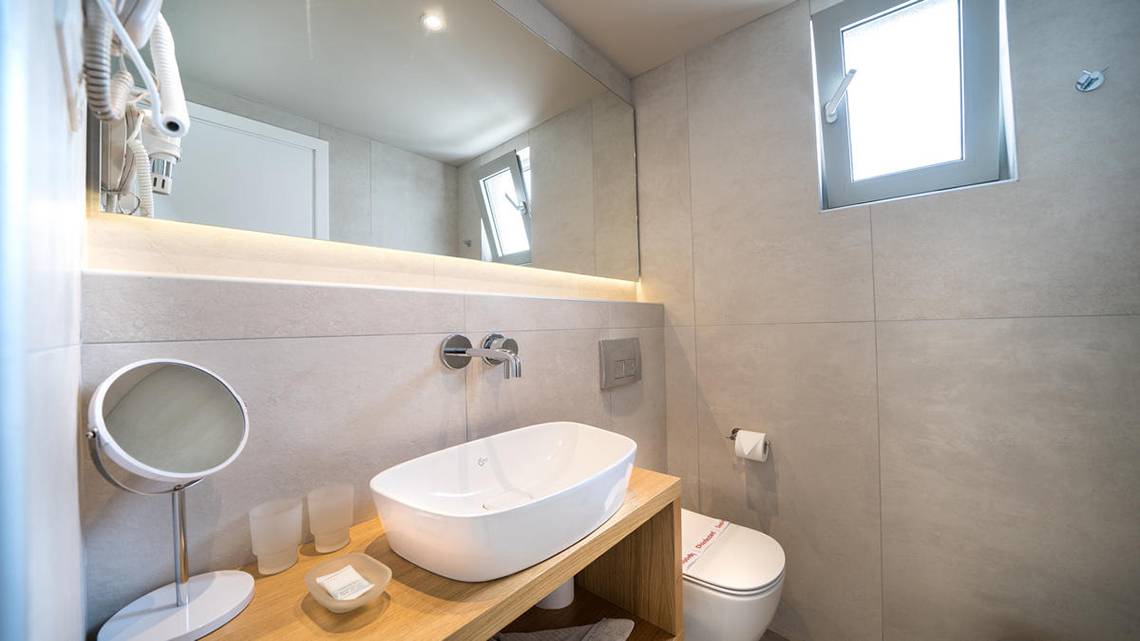 Badezimmer im Adele Beach Hotel mit Waschbecken, Spiegel, Toilette und Fenster.
