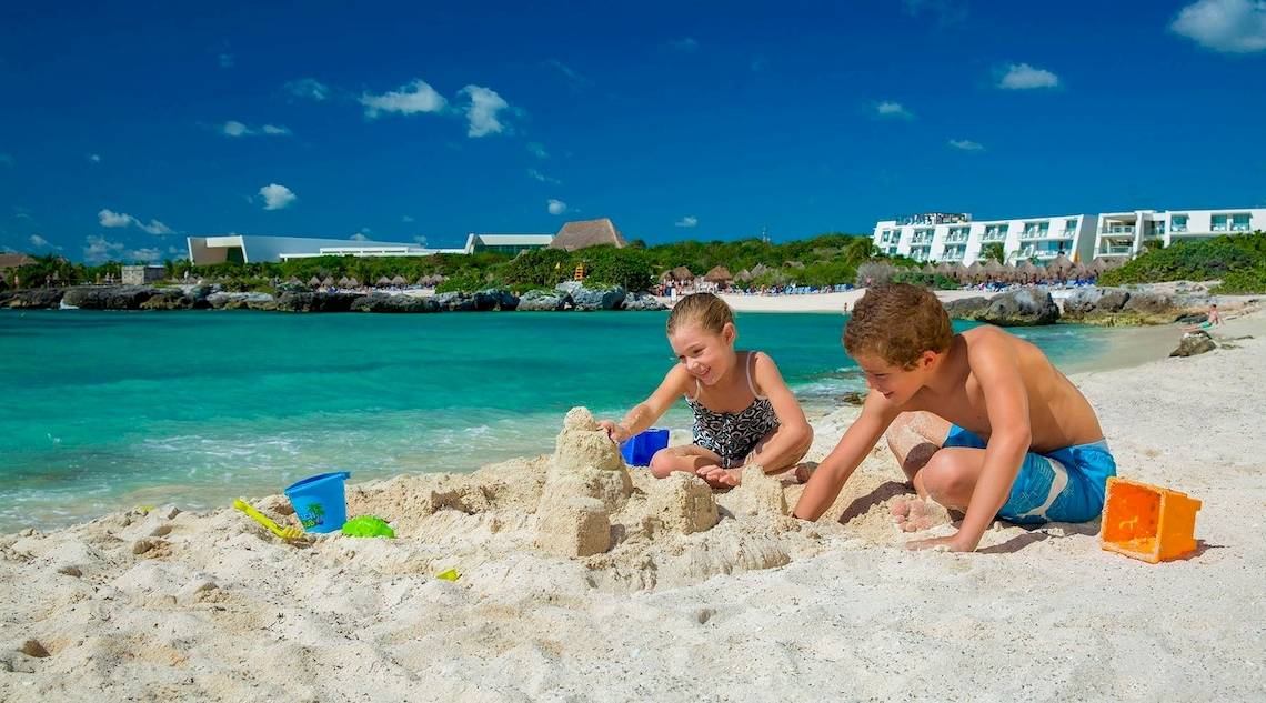 Zwei Kinder bauen am Strand des Grand Sirenis Riviera Maya Resorts und Spa einen Sandburg