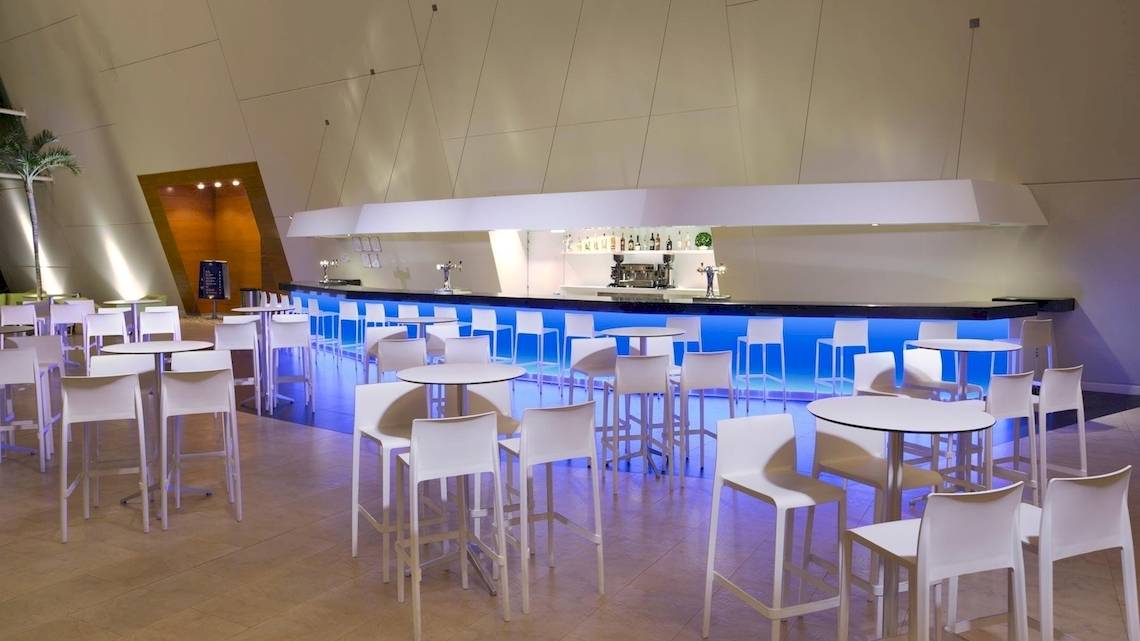 Barbereich im Grand Sirenis Riviera Maya Resort & Spa mit weißen Stühlen und blauen Leuchtlichtern.