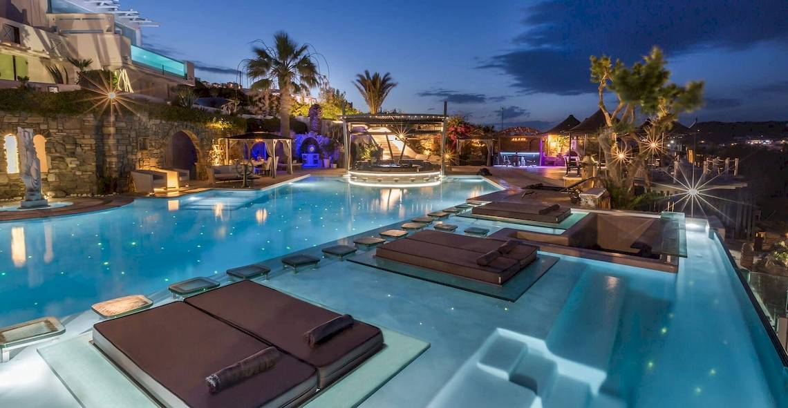 Der Pool des Kivotos Mykonos Hotels bei Nacht mit Lounge-Liegestühlen und beleuchteten Wasserflächen.