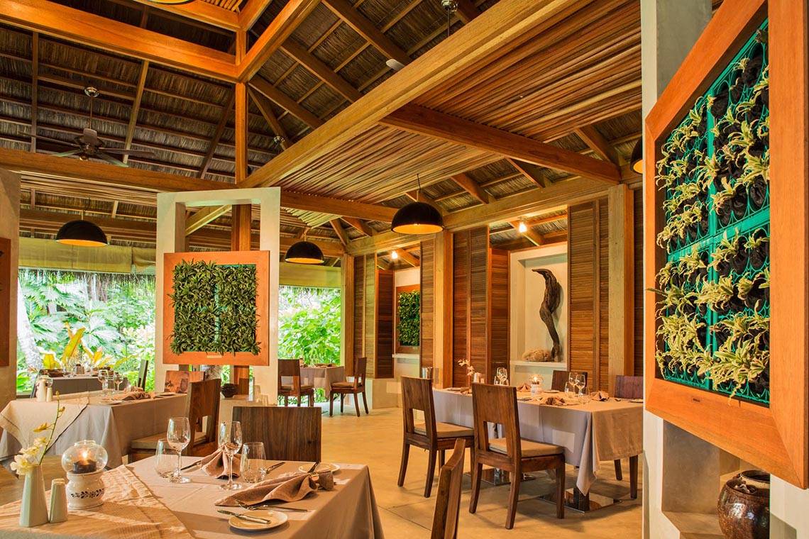 Innenbereich des Kuramathi Maldives Hotel mit Esstischen und hängenden Lampen.