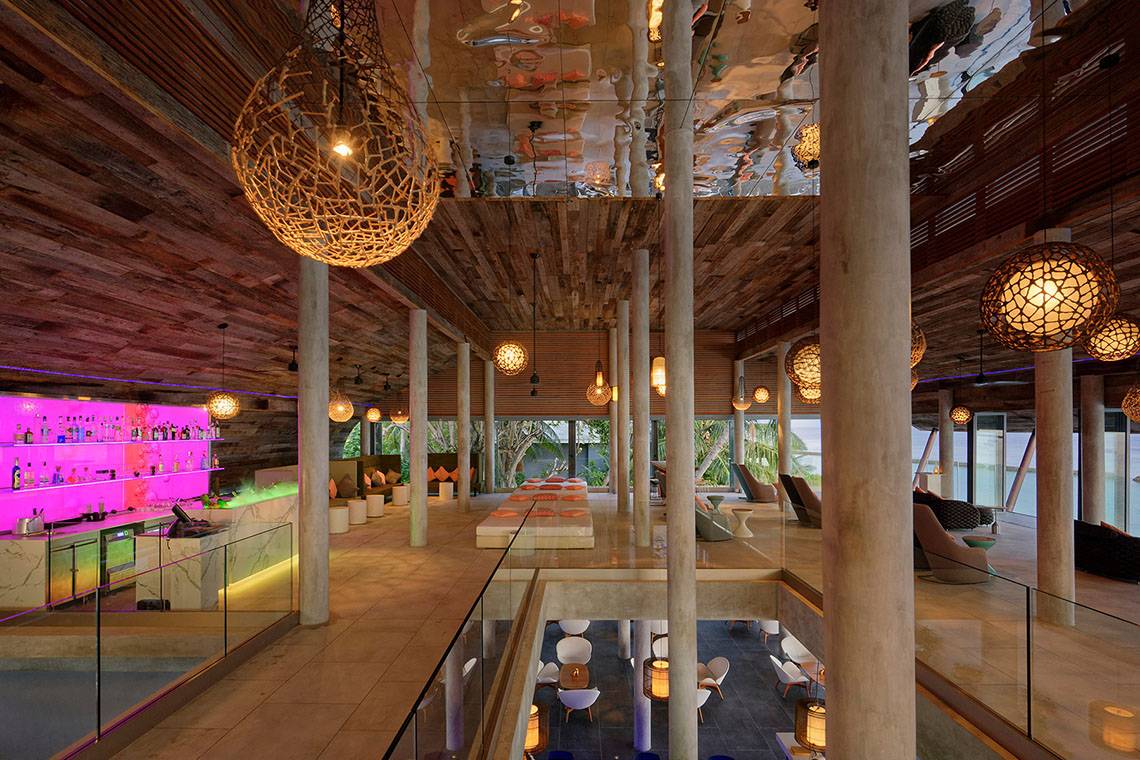 Innenbereich des Kuramathi Maldives Hotels mit Holzdecke, gespiegelter Decke, Sitzbereich und Bar.
