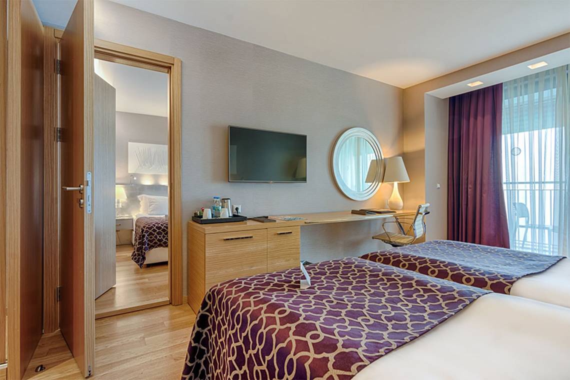 Innenansicht eines Doppelzimmers im Akra Hotel mit zwei Betten, Schreibtisch und Fernseher.