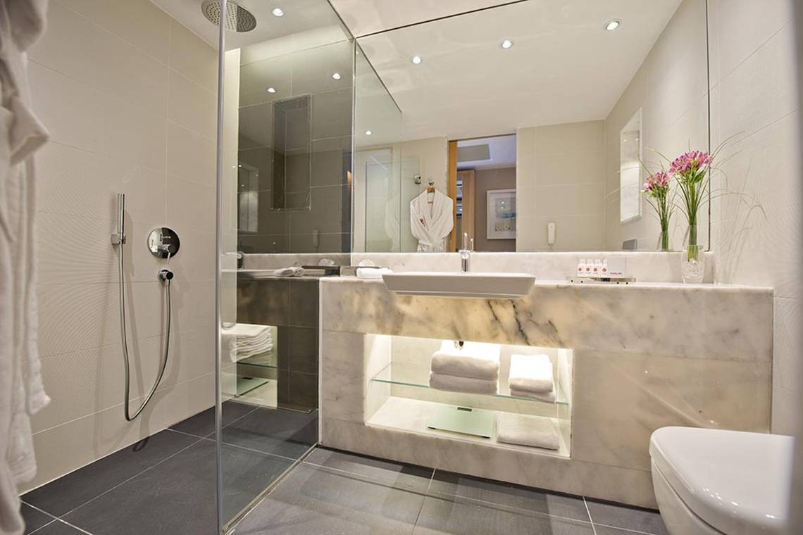 Das elegante Badezimmer des Akra Hotels mit einer großen Glasdusche und einem Marmorwaschtisch.