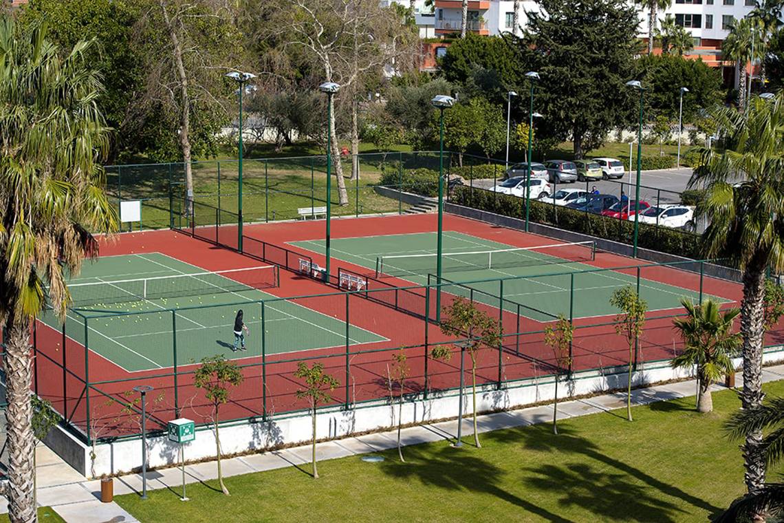 Tennisplatz im Freien Bereich des Akra Hotels mit einem Spieler, der Tennis spielt.