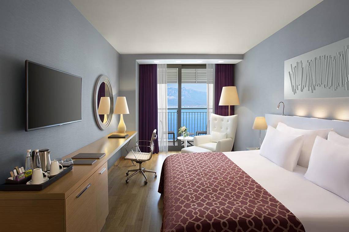 Innenansicht des Akra Hotels, Zimmer mit Meerblick, modernes Dekor, große Fenster, Blick auf das Meer und Berge.
