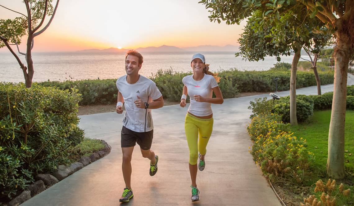 Zwei Menschen joggen auf einem Weg am Strand bei Sonnenuntergang im Xanadu Island Bodrum.