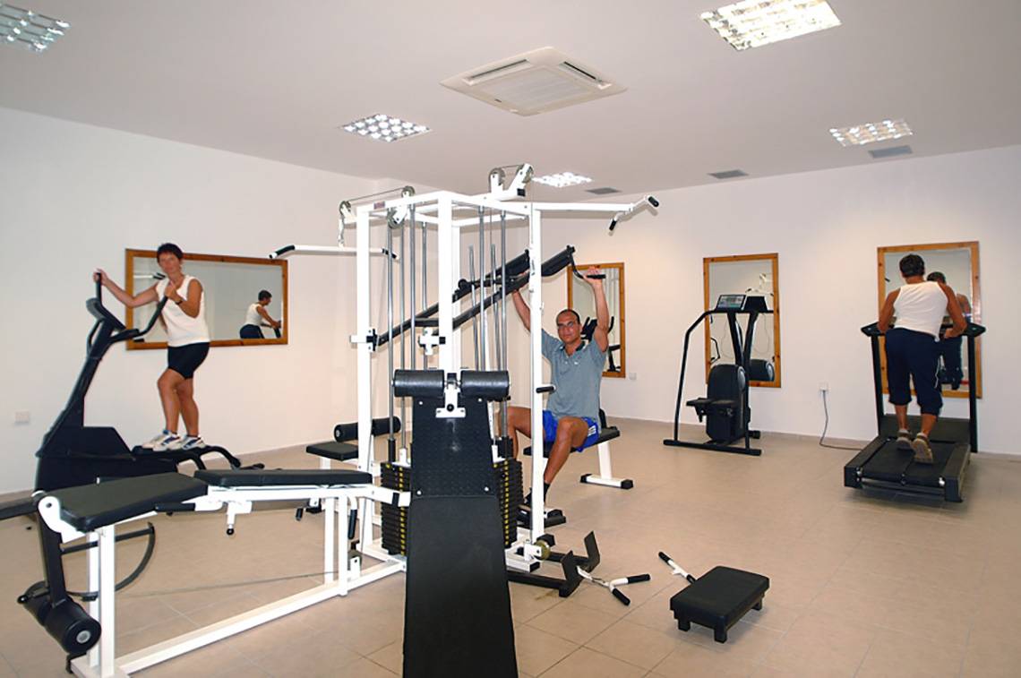 Fitnessraum im Themis Beach Hotel mit Personen auf Laufband und Kraftgeräten.