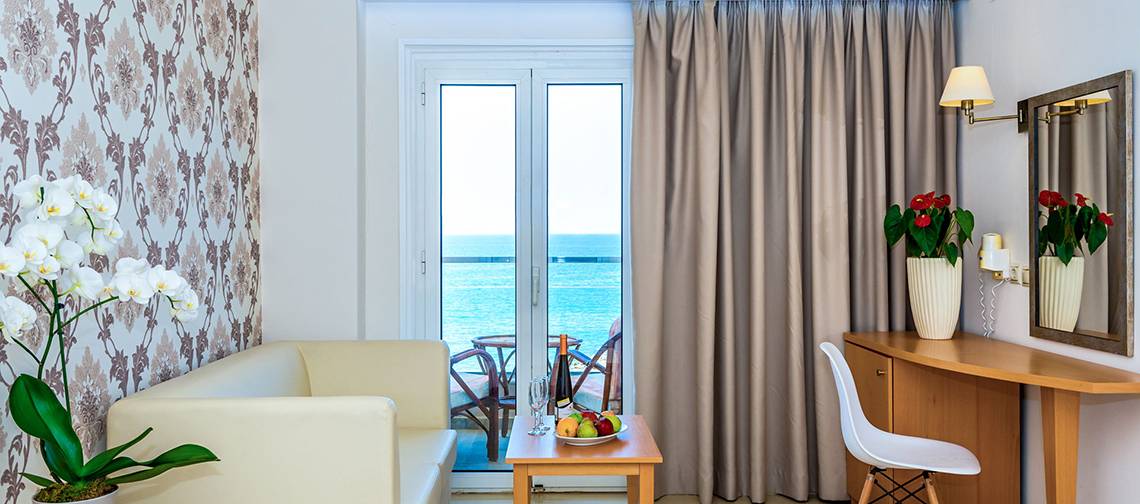 Hotelzimmer mit Meerblick, Sofa, Tisch mit Obst, und Balkontür offen