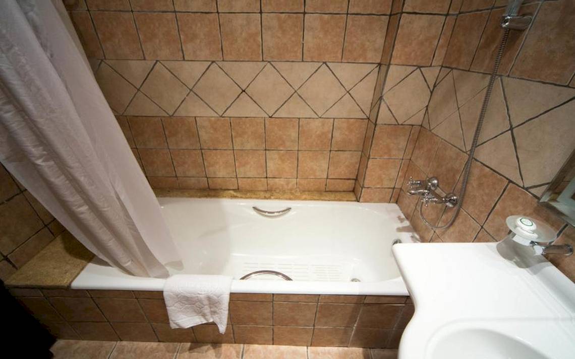 Ein Badezimmer mit einer Badewanne, einer weißen Dusche, braunen Fliesen und einem Spiegel.