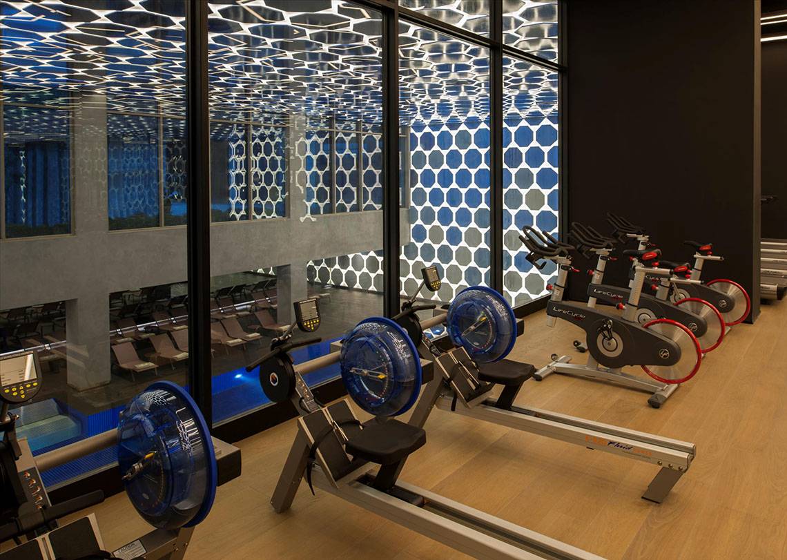 Fitness-Center im Maxx Royal Kemer Resort mit gemusterter Decke und Reihe von Crosstrainern.