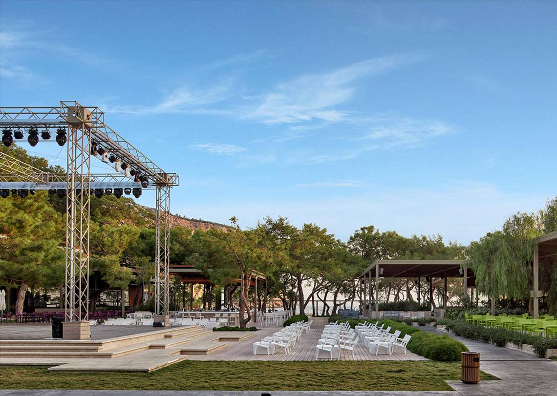 Maxx Royal Kemer Resort Freiluft-Veranstaltungsort mit Bühnenaufbau, weißen Stühlen und grünen Tischen.