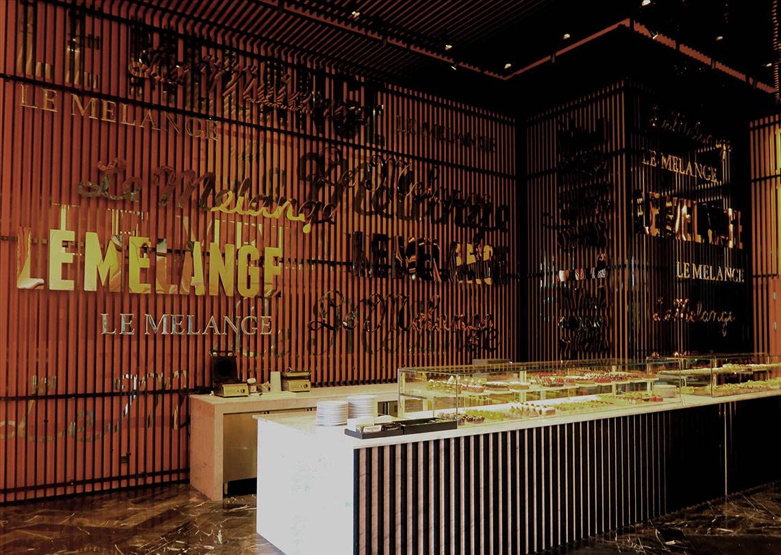 Innenansicht des Le Melange Cafés im Maxx Royal Kemer Resort mit dekorierten Wänden und einer Theke voller Desserts.