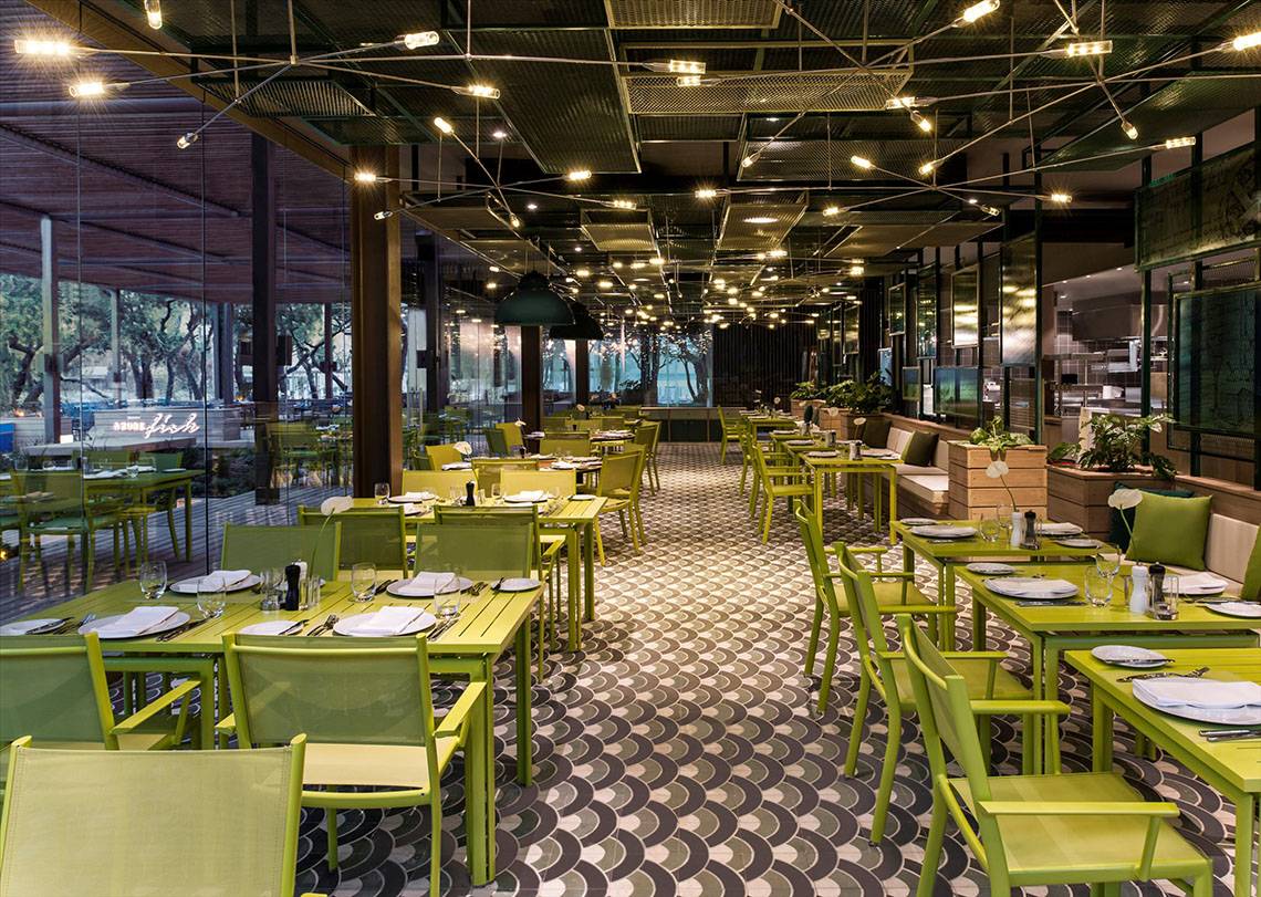 Innenbereich des Restaurants im Maxx Royal Kemer Resort mit grünen Tischen und Stühlen.