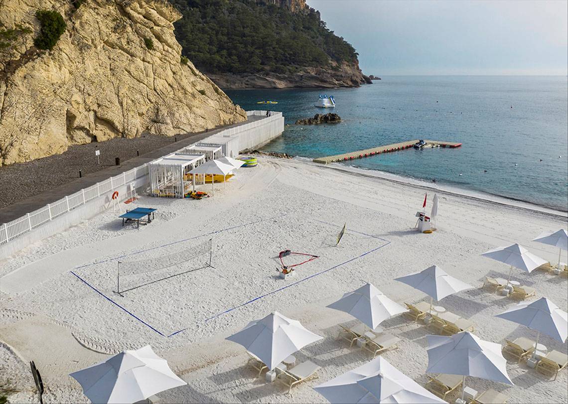 Strandvolleyballplatz am Maxx Royal Kemer Resort mit weißen Sonnenschirmen und Liegestühlen.