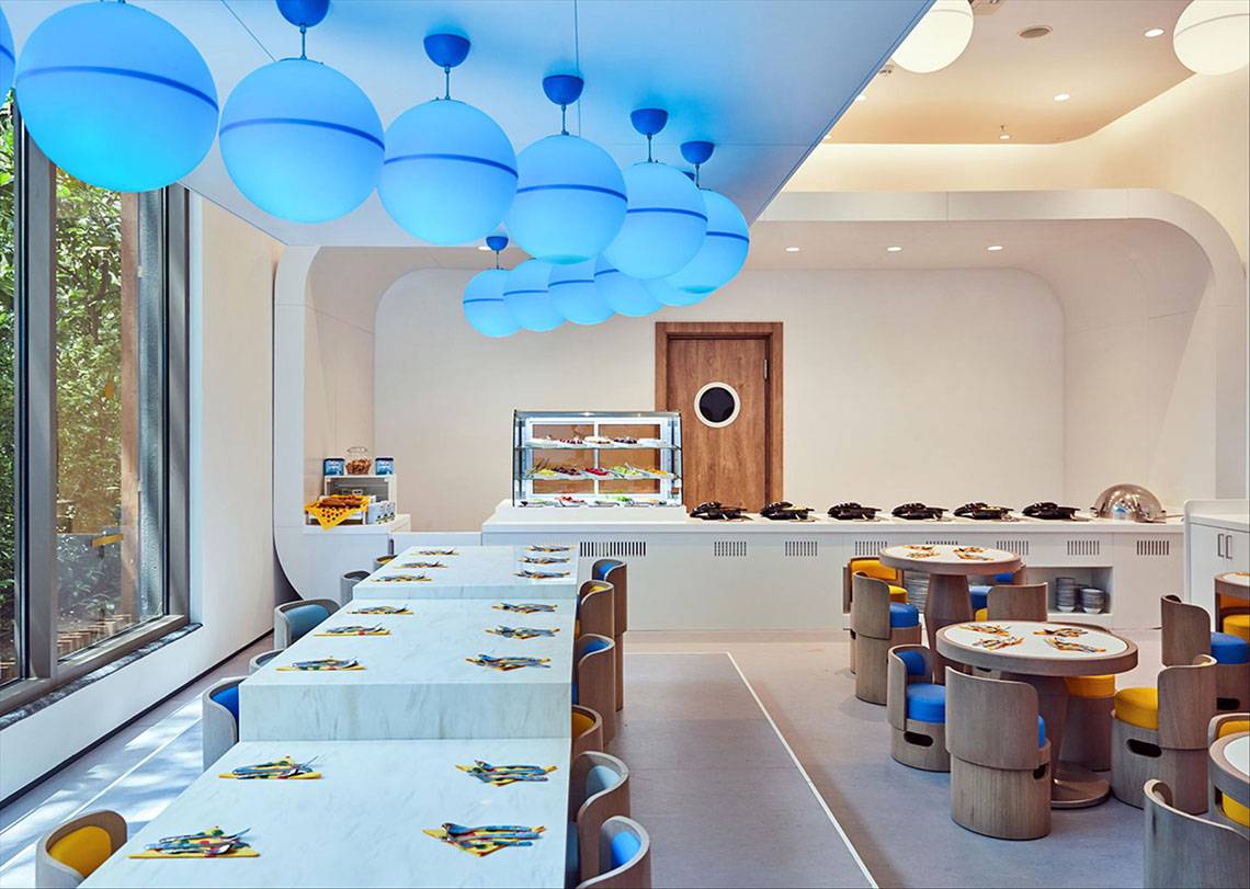 Innenbereich des Maxx Royal Kemer Resorts mit langen Tischen, runden Stühlen und blauen Pendelleuchten.